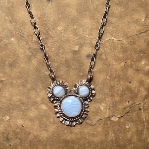 May include: A necklace featuring a copper chain and a pendant with three round, light blue, banded agate stones set in copper. The stones are arranged in a cluster, with one large stone at the bottom and two smaller stones above, all framed by textured copper metalwork.