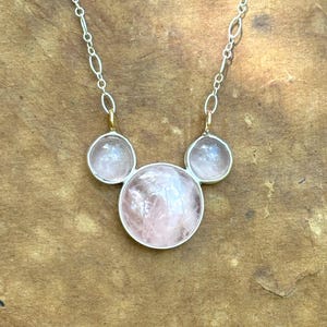 Puede incluir: Un collar de plata con tres piedras preciosas redondas de color rosa claro. Las piedras est&aacute;n engastadas en biseles de plata y unidas por una delicada cadena de plata. El collar tiene un dise&ntilde;o minimalista y un acabado pulido.