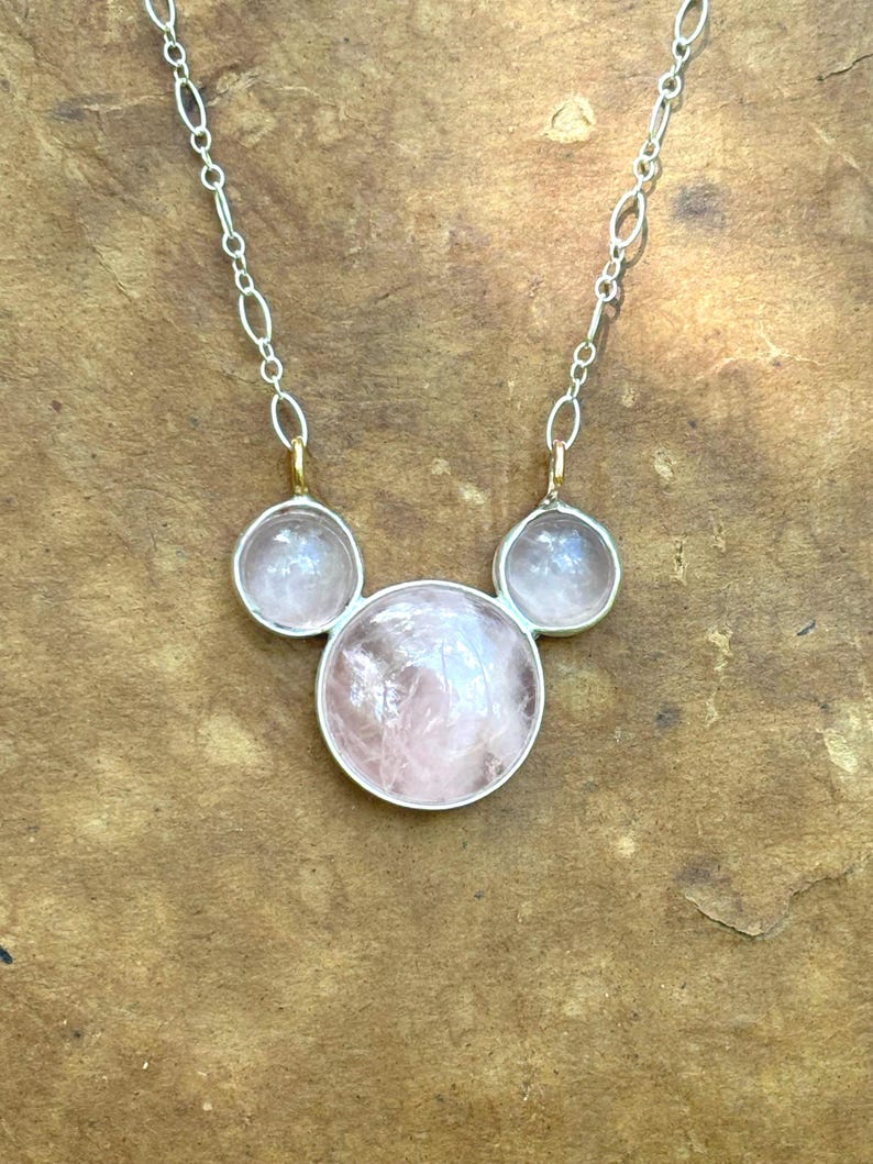 Puede incluir: Un collar de plata con tres piedras preciosas redondas de color rosa claro. Las piedras est&aacute;n engastadas en biseles de plata y unidas por una delicada cadena de plata. El collar tiene un dise&ntilde;o minimalista y un acabado pulido.
