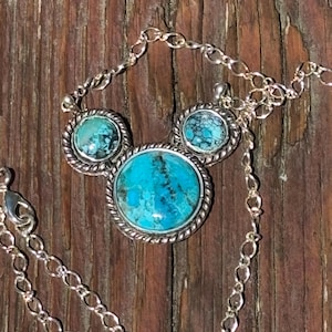 Pu&ograve; includere: Un set di collana e orecchini in argento con pietre color turchese. La collana ha un grande pendente rotondo e due orecchini pi&ugrave; piccoli, tutti con un bordo argentato a forma di corda. La catena &egrave; a maglie delicate.
