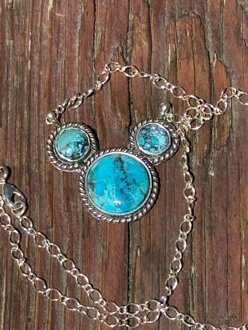 Pu&ograve; includere: Un set di collana e orecchini in argento con pietre color turchese. La collana ha un grande pendente rotondo e due orecchini pi&ugrave; piccoli, tutti con un bordo argentato a forma di corda. La catena &egrave; a maglie delicate.