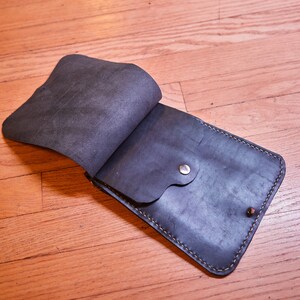 May include: A black leather crossbody bag with a flap closure and a small pocket on the front. The bag has a stitched edge and a silver metal button.