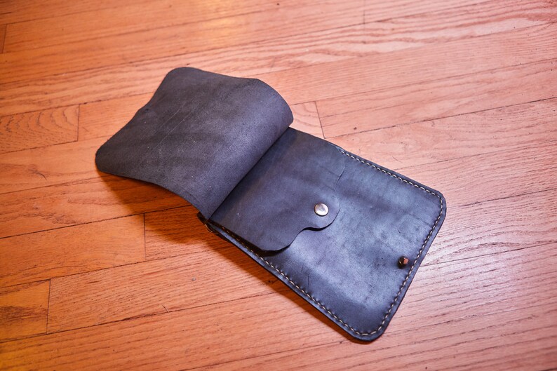 May include: A black leather crossbody bag with a flap closure and a small pocket on the front. The bag has a stitched edge and a silver metal button.