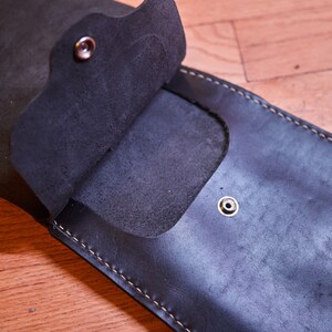 May include: A black leather wallet with a flap that opens to reveal a pocket. The wallet has a stitched edge and three metal snaps.