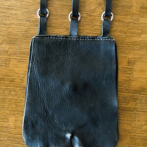 May include: A black leather pouch with three hanging loops and silver metal rings. The pouch has a worn, distressed look.