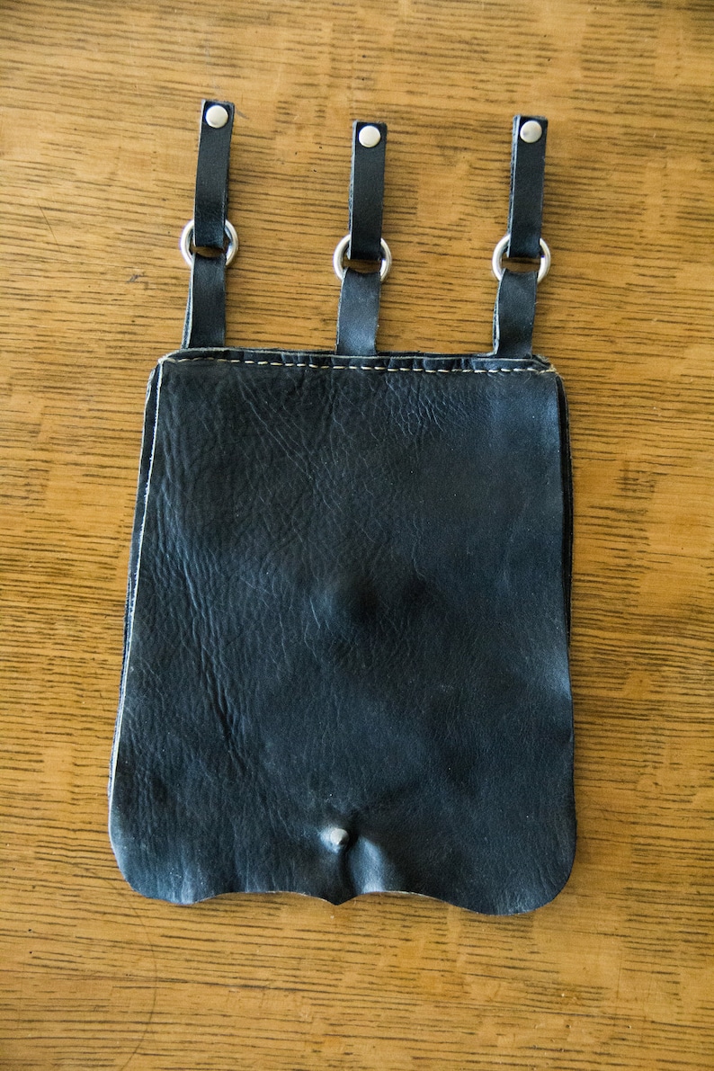 May include: A black leather pouch with three hanging loops and silver metal rings. The pouch has a worn, distressed look.