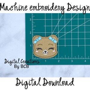May include: A machine embroidery design featuring a smiling bear face with blue bows, eyelashes, and rosy cheeks. The design is on a green cutting mat with measurements in inches. Text includes "Machine embroidery Design", "Digital Creations By BCB", and "Digital Download".
