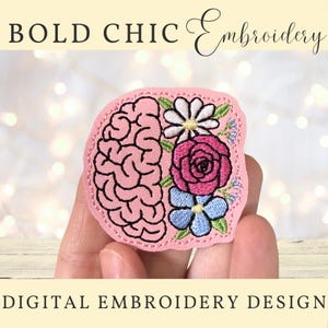 Pode incluir: Um emblema bordado apresentando um cérebro rosa no lado esquerdo e um grupo de flores incluindo uma margarida branca, uma rosa rosa-escura e flores azul-claras no lado direito, sobre um fundo rosa claro com bordas costuradas.