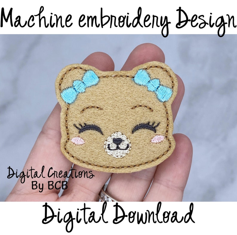 May include: Machine embroidery design of a smiling bear face with blue bows, eyelashes, and pink cheeks. The bear is tan with brown stitching. Text reads "Machine embroidery Design", "Digital Creations By BCB", and "Digital Download".
