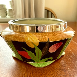 May include: A vintage ceramic bowl with a silver rim and a floral design featuring tulips in shades of yellow, red, and pink. The bowl has a geometric shape with a black background and green accents.