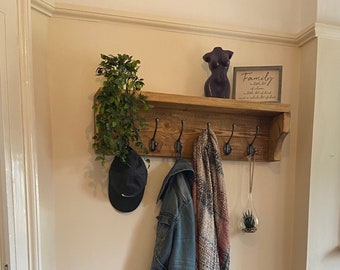 May include: A wooden coat rack with hooks and a shelf, featuring a green plant, a black hat, a blue denim jacket, and a pink and white scarf. Below the rack is a wooden shoe rack with two shelves, holding a variety of shoes. The sign on the rack reads "Family is not an important thing. It's everything."