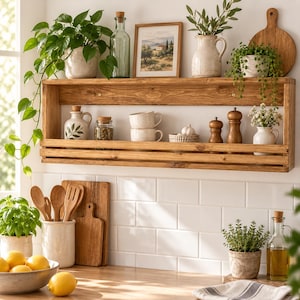 Puede incluir: Un estante de pared de madera con dos niveles horizontales. El nivel superior sostiene una planta en maceta, una botella de vidrio, un cuadro, una jarra de cerámica y una tabla de cortar. El nivel inferior contiene frascos, tazas y molinillos.