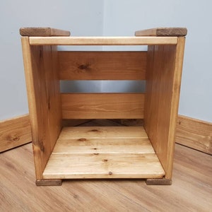 May include: A wooden storage cube with two shelves. The cube is made of natural wood and has a light brown finish.