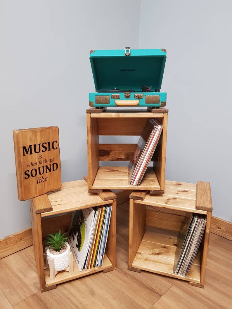 May include: Three wooden crates with shelves, each holding vinyl records. A teal record player sits on top of the crate in the center. A wooden sign reads "MUSIC what is feelings SOUND like".