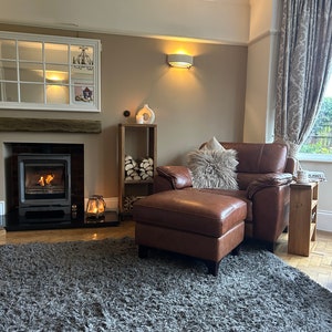 May include: A brown leather armchair with a fluffy white throw pillow and a matching ottoman. The armchair is in front of a fireplace with a lit fire. A gray shag rug covers the floor.