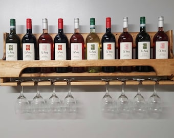 Pode incluir: Um suporte de vinho de parede de madeira com uma prateleira para garrafas e uma prateleira inferior para copos de vinho. O suporte contém 10 garrafas de vinho e 8 copos de vinho. As garrafas são etiquetadas com "Ga Nova".