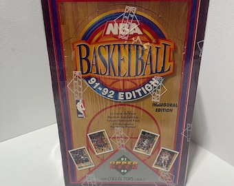 May include: A sealed box of 1991-92 Upper Deck NBA Basketball cards. The box features a basketball court design with the NBA logo and the text "BASKETBALL 91-92 EDITION". It includes 12 cards per pack and is tamper-resistant.