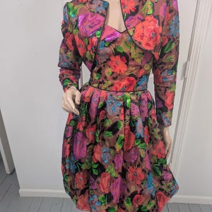 May include: A vintage floral dress and matching bolero jacket. The dress features a sweetheart neckline and a pleated skirt. The sheer jacket has long sleeves and a rounded collar. The fabric is a mix of red, pink, purple, and blue flowers on a black background.