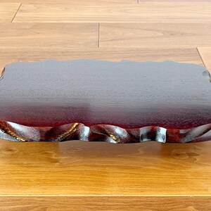 May include: A rectangular, dark red wooden tray with a natural, wavy edge. The tray has a glossy finish and appears to be made of a single piece of wood. The tray is approximately 30 cm long and 20 cm wide.