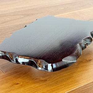 May include: A dark brown wooden tray with an organic, irregular shape and a glossy finish. The tray has a smooth surface and a wavy edge. The wood grain is visible. This tray is likely for serving or display, and is approximately 30 cm in length.