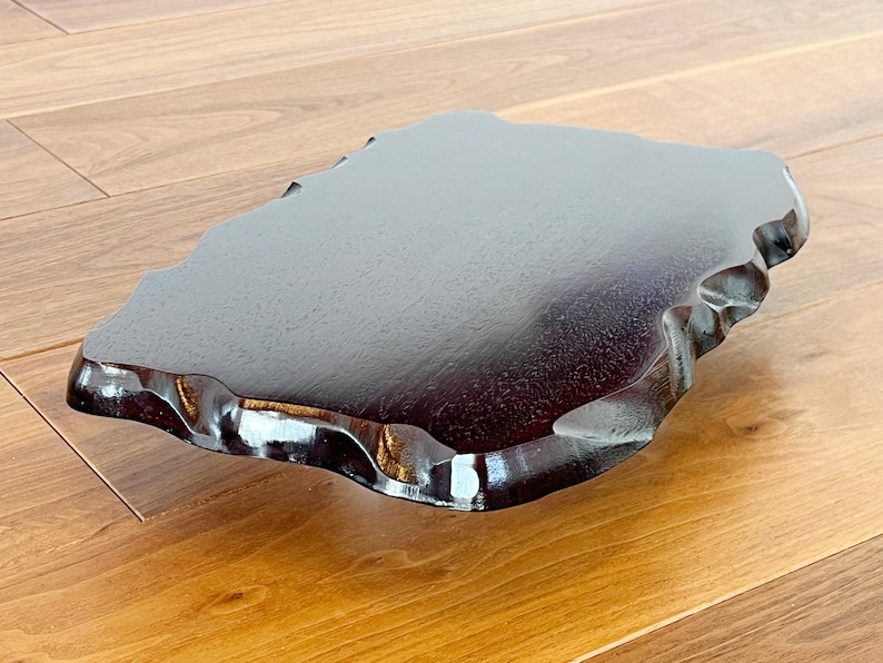 May include: A dark brown wooden tray with an organic, irregular shape and a glossy finish. The tray has a smooth surface and a wavy edge. The wood grain is visible. This tray is likely for serving or display, and is approximately 30 cm in length.