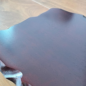 May include: Close-up of a dark brown wooden table with an unusual, organic shape. The table has a smooth, polished surface and a natural wood grain pattern. The edges of the table are gently curved.