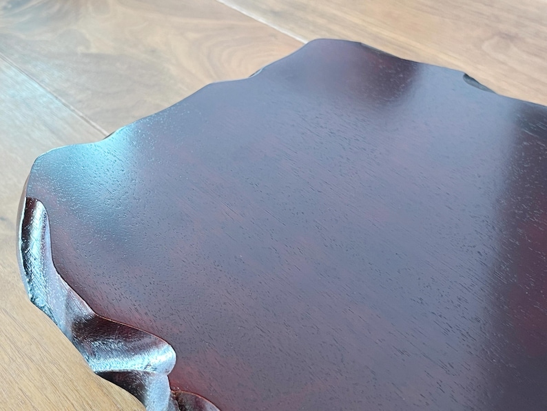 May include: Close-up of a dark brown wooden table with an unusual, organic shape. The table has a smooth, polished surface and a natural wood grain pattern. The edges of the table are gently curved.