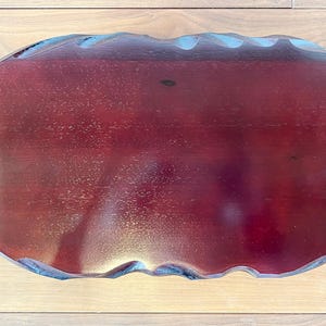 May include: A rectangular, wooden serving tray with a deep burgundy finish. The edges have a wavy, scalloped design, and the tray sits on a light-coloured wooden surface. The tray's dimensions are not visible.