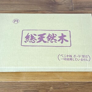 May include: A rectangular, light beige box with Japanese text in a purple rectangle. The text reads "Total Natural Wood". A small circular symbol is in the upper left corner. The box is on a wooden surface.
