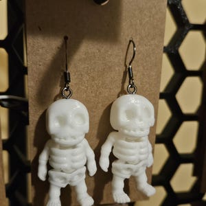 May include: A pair of white skeleton earrings with silver hooks. The skeletons are small and detailed, with visible ribs and skulls.