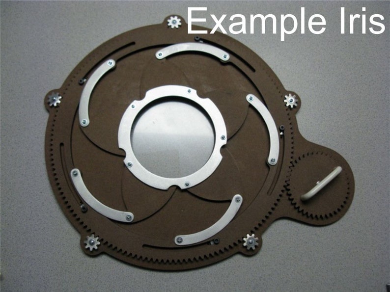 Puede incluir: Un diafragma de iris de c&aacute;mara de madera marr&oacute;n con l&aacute;minas y engranajes de metal. El iris est&aacute; abierto y las l&aacute;minas son visibles. El iris est&aacute; etiquetado como "Example Iris".