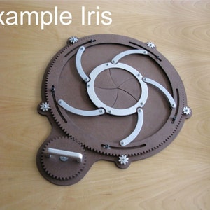 Puede incluir: Un diafragma de iris circular de madera marr&oacute;n con brazos y engranajes de metal plateado. El iris est&aacute; abierto y los brazos est&aacute;n extendidos. El iris est&aacute; sobre una superficie de madera.