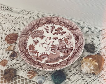 Puede incluir: Un plato de cerámica rojo y blanco con un diseño chino tradicional. El plato está sobre una superficie de crochet blanco con conchas y piedras.