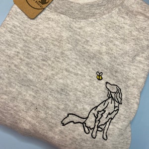 May include: A heather gray sweatshirt featuring an embroidered black dog looking up at a yellow and black bee. A brown tag with the text "Maisie & Murphy" is attached to the sweatshirt.