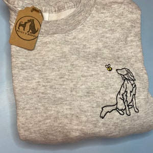 May include: A heather gray sweatshirt with a black embroidered dog and yellow bee design. The dog is looking up at the bee. A brown tag with the text "Maisie & Murphy" is attached to the sweatshirt.