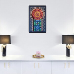 May include: A white cabinet with two doors and gold handles. The cabinet is decorated with two black lamps with black lampshades and a tray with a pink box on top. A framed artwork with a colourful mandala design hangs on the wall above the cabinet.