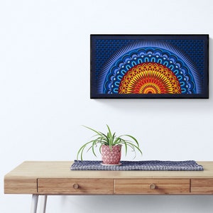Op de afbeelding: Een rechthoekig wandkunstwerk met een gelaagd, halfrond mandala-ontwerp in levendige tinten geel, oranje, rood en blauw, geplaatst in een zwarte lijst. Het kunstwerk toont ingewikkelde geometrische patronen en concentrische ringen.