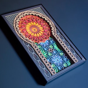 May include: A colourful paper art piece with a geometric design. The artwork features a large, red and yellow flower in the centre, surrounded by smaller blue flowers and intricate patterns. The piece is framed in black.