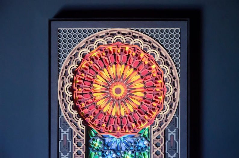 May include: A colourful paper art piece with a red, yellow and orange mandala design. The mandala is surrounded by a geometric pattern in shades of brown and grey.