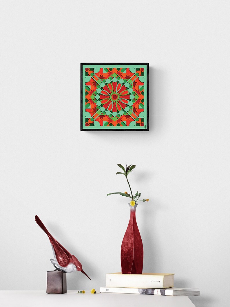 May include: A framed geometric art print with a red, green, and orange pattern. The print is hanging on a white wall above a red vase with a green plant and a red bird figurine.
