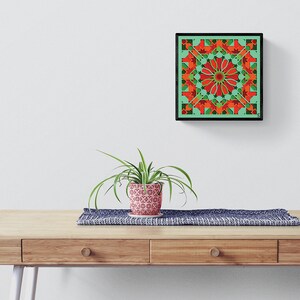 May include: A framed geometric art print with a green background and red and orange geometric shapes. The print is hanging on a white wall above a wooden table with a plant in a patterned pot.