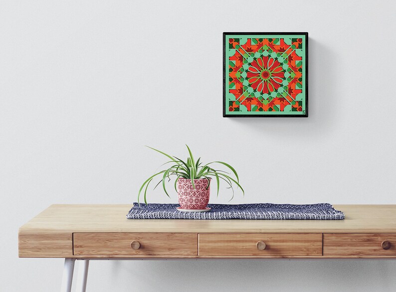 May include: A framed geometric art print with a green background and red and orange geometric shapes. The print is hanging on a white wall above a wooden table with a plant in a patterned pot.
