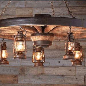 May include: Rustic wagon wheel chandelier with eight hanging oil lanterns. The lanterns have clear glass and are lit with warm, inviting light. The wheel is made of wood and metal, creating a vintage aesthetic.