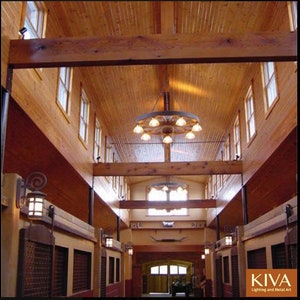 Puede incluir: Vista interior de un pasillo con techo y paredes de madera. Una gran l&aacute;mpara de ara&ntilde;a con forma de rueda de carro cuelga del techo, iluminando el espacio. Peque&ntilde;as ventanas bordean las paredes y se montan apliques decorativos. El dise&ntilde;o general tiene un tema r&uacute;stico y occidental.