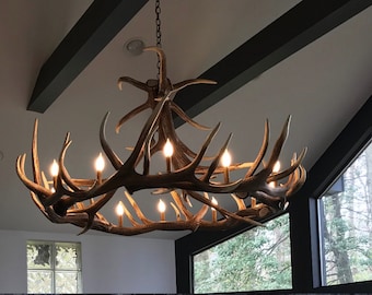 May include: A large antler chandelier with multiple light bulbs hanging from a chain. The chandelier is made of natural antlers and has a rustic, lodge-style aesthetic.