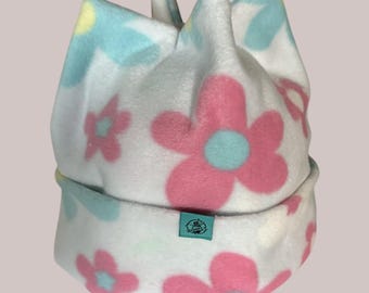 May include: A white fleece hat with a floral pattern. The flowers are pink with light blue centers and light blue and yellow accents. A small teal tag is sewn on the brim.
