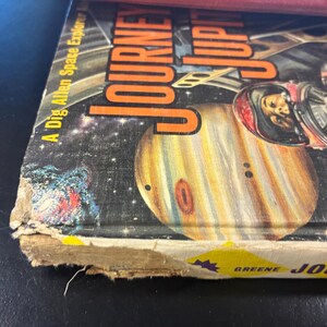 Op de afbeelding: Vintage boekomslag getiteld "Journey to Jupiter" met een illustratie van Jupiter en een astronaut. De omslag heeft een ruimtethema met planeten en sterren, en de titel is oranje.