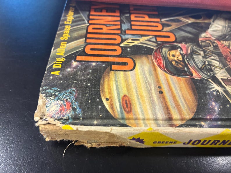 Op de afbeelding: Vintage boekomslag getiteld "Journey to Jupiter" met een illustratie van Jupiter en een astronaut. De omslag heeft een ruimtethema met planeten en sterren, en de titel is oranje.