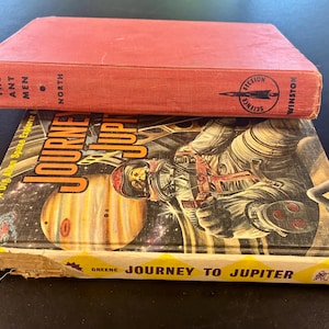 Op de afbeelding: Twee vintage sciencefictionboeken. Het bovenste boek is rood met de titel "The Ant Men" en de uitgever "Winston". Het onderste boek heet "Journey to Jupiter" met een illustratie van een astronaut en de planeet Jupiter.