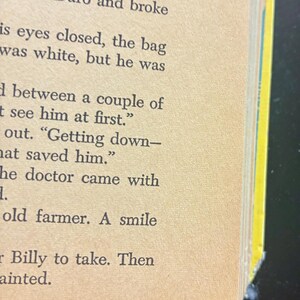 Op de afbeelding: Close-up van pagina's van een vintage boek, met zwarte tekst gedrukt op verouderd, vergeeld papier. De hoek van het boek is gescheurd, wat slijtage aantoont. De randen zijn geel en blauw.